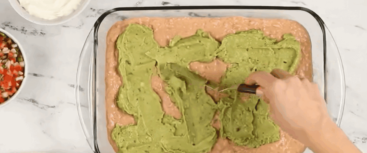 Spreading guacamole over the bean layer.