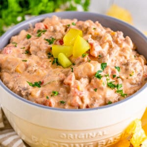 Cheeseburger dip in a white bowl topped with dill pickles