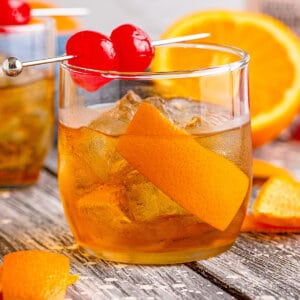 Side view of an old fashioned cocktail with orange peel and cherries