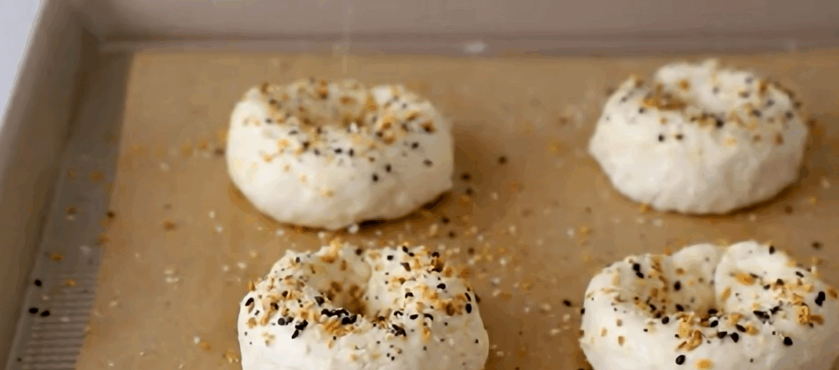 Four bagels topped with everything bagel seasoning on a lined baking sheet.
