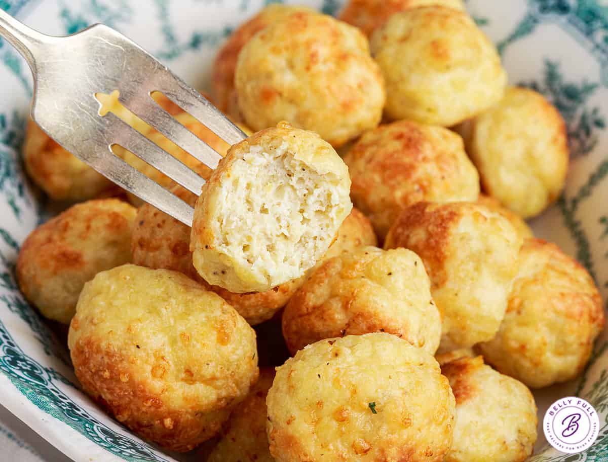 A fork holding a chicken meatball with a bite missing over a bowl of other meatballs