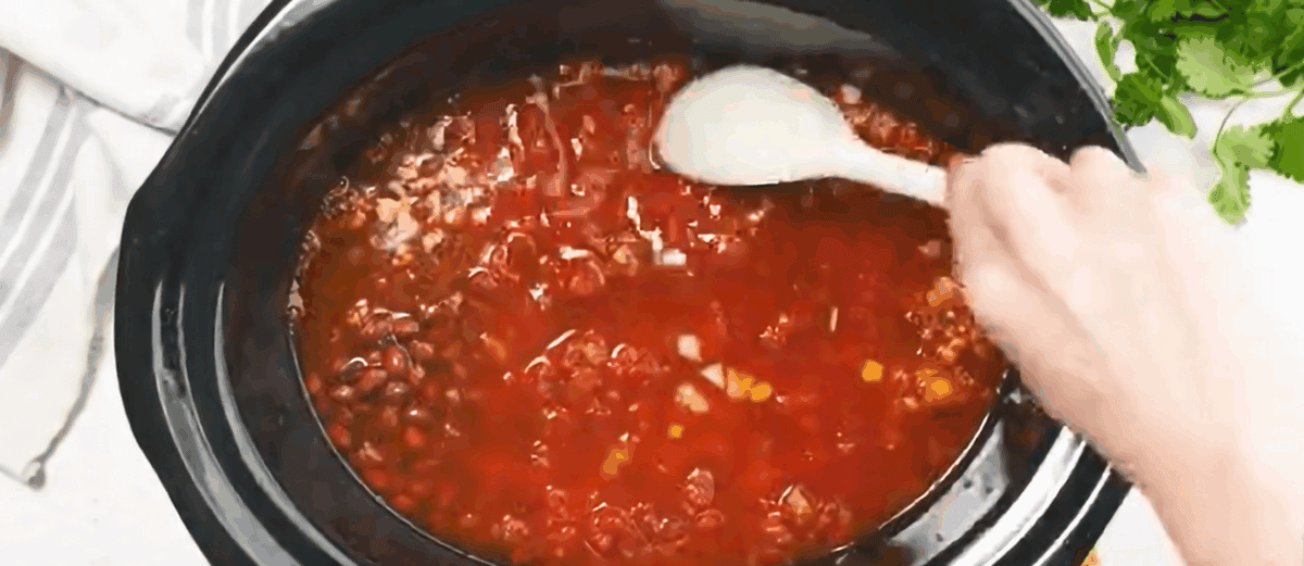 Combining the ingredients to make chicken taco soup in a black crockpot.