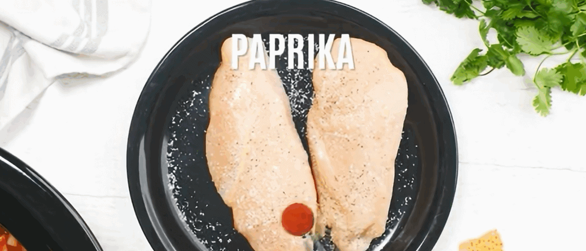 Seasoning chicken breasts on a black plate. 