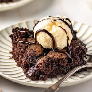 Angled view of chocolate cobbler topped with vanilla ice cream on a white plate