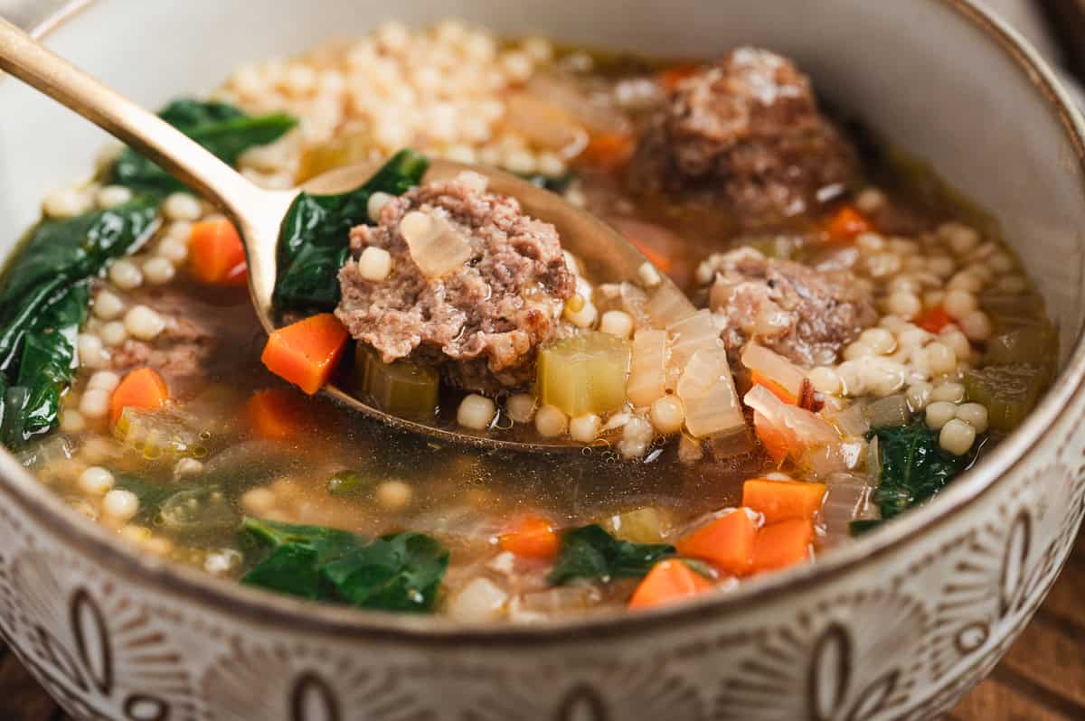 Close up of spoonful of Italian wedding soup showing meatball, pasta, spinach, and vegetables in broth