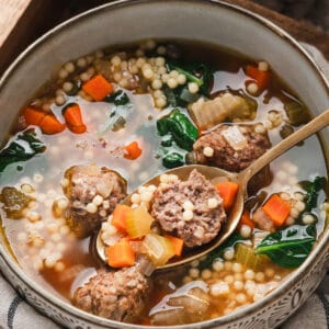 Bowl of Italian wedding soup with meatballs, acini di pepe pasta, spinach, carrots, and onions in a clear savory broth
