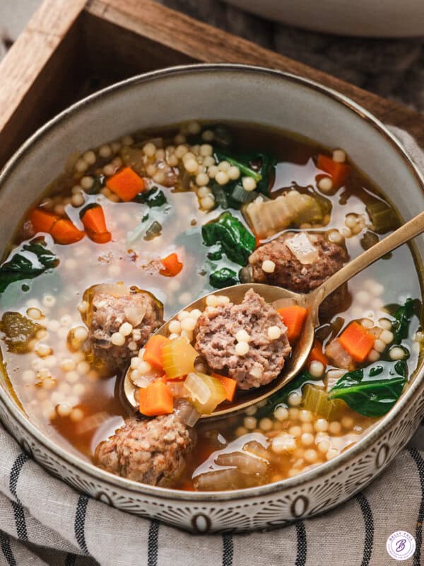 Bowl of Italian wedding soup with meatballs, acini di pepe pasta, spinach, carrots, and onions in a clear savory broth