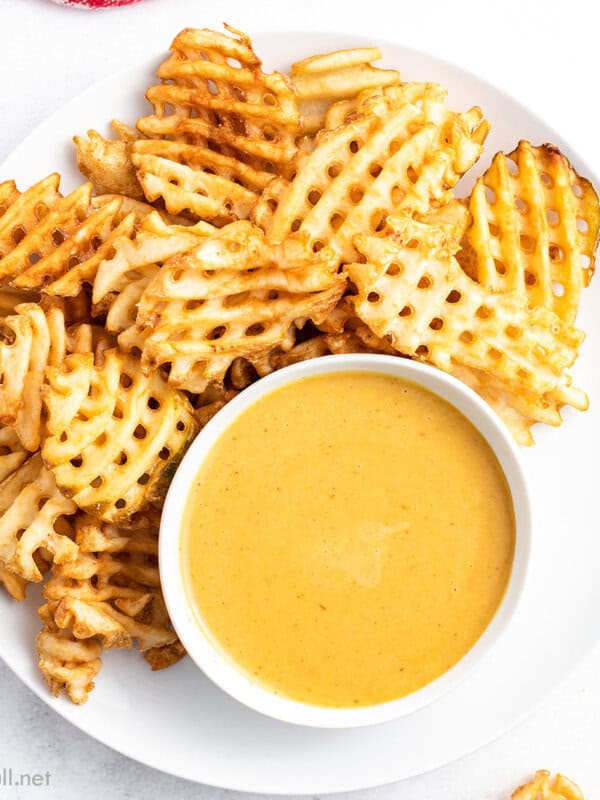 Waffle fries and a dish of chick-fil-a sauce on a white plate