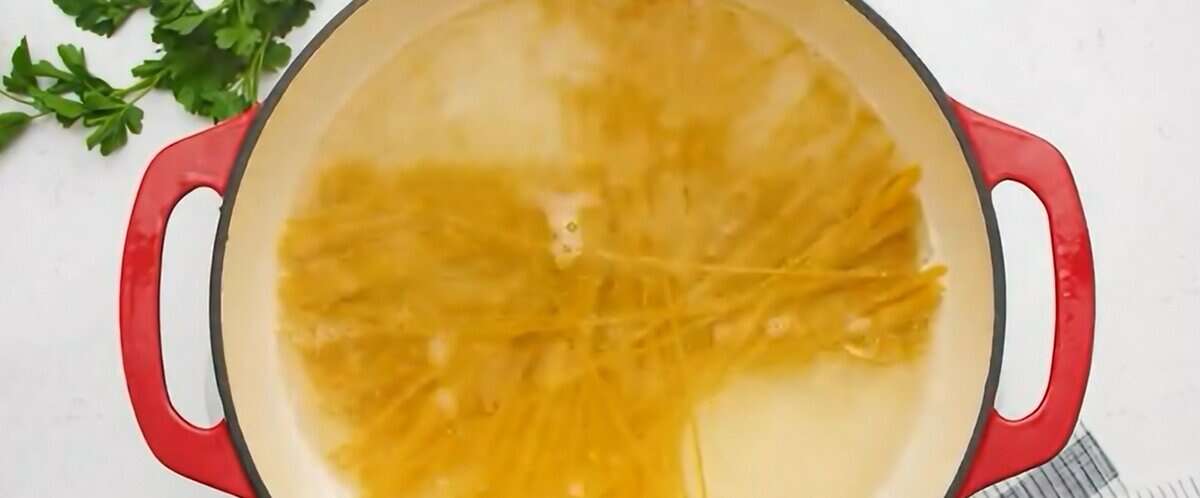 Boiling spaghetti in a pot with red handles.