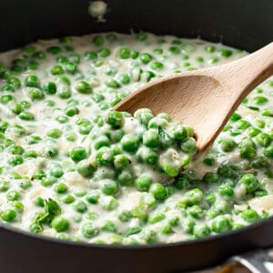 close up creamed peas on wooden spoon in pan