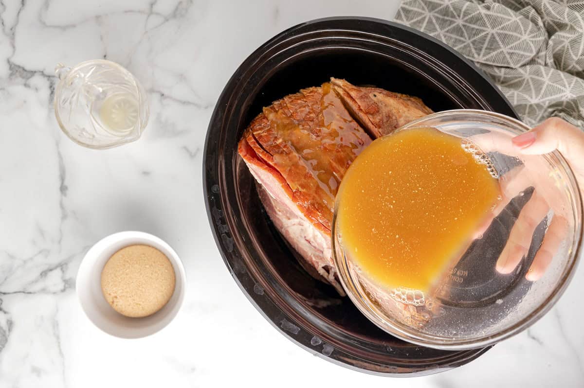 sauce being poured over spiral ham in crockpot