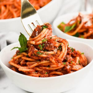 A fork twirling noodles in a bowl of spaghetti and meat sauce