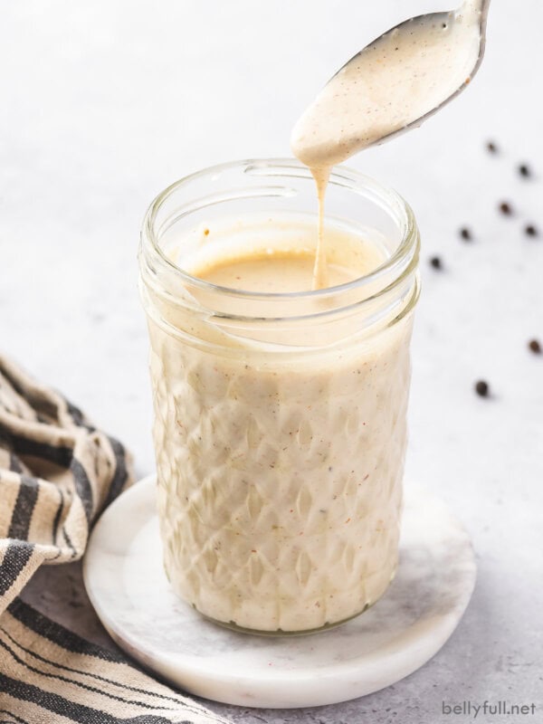 A glass jar with a spoon of Alabama white sauce above it