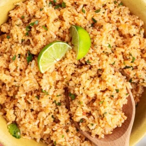 A wooden spoon stirring a bowl of Mexican rice