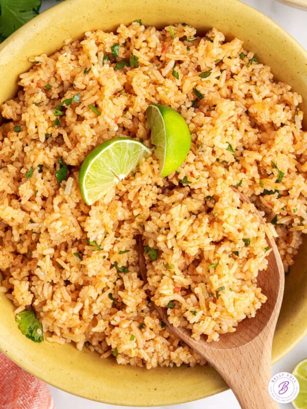A wooden spoon stirring a bowl of Mexican rice