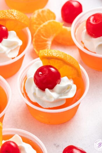 sex on the beach jello shots garnished with whipped cream, orange wedge, and maraschino cherry