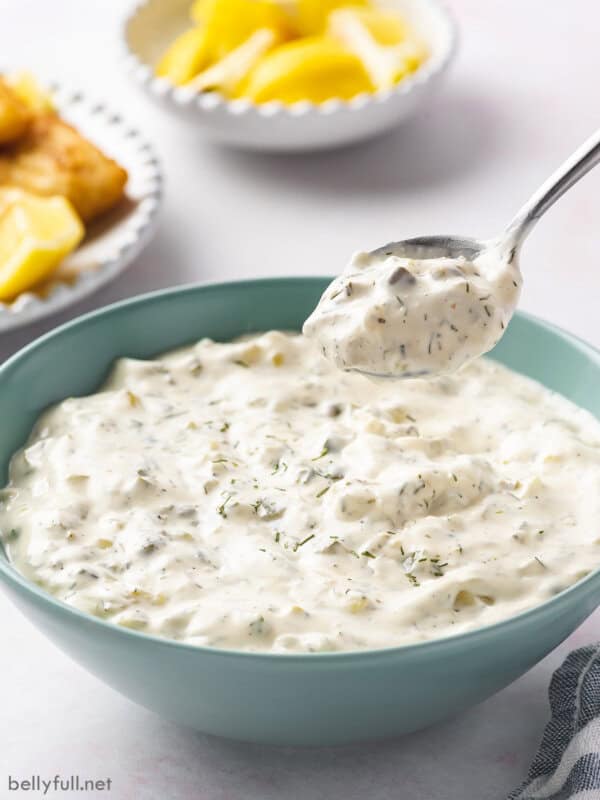 Angled overhead view of bowl of tartar sauce with a spoon above it