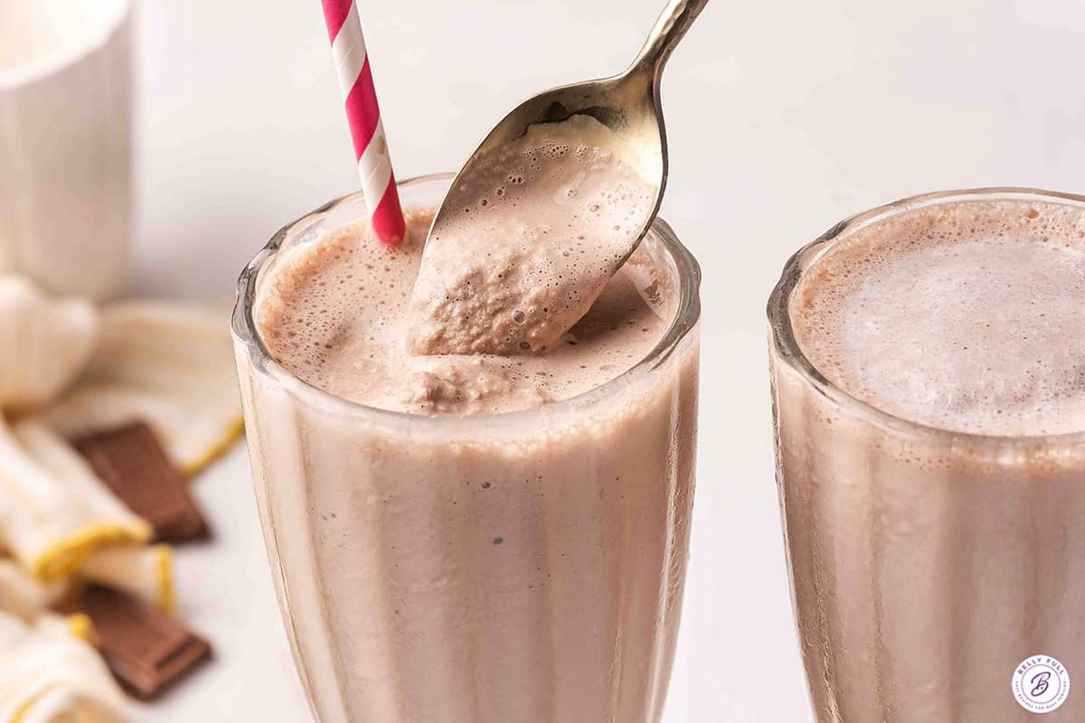 Close-up of a gold spoon scooping thick, creamy homemade Wendy's Frosty from a tall glass with a pink striped straw