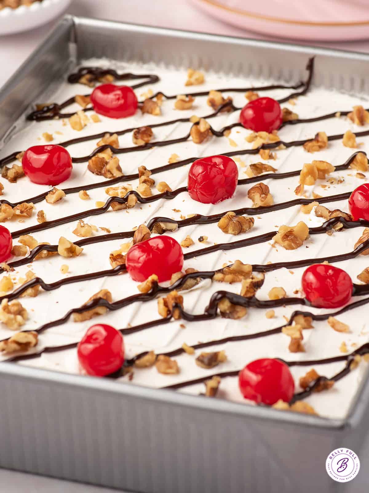 lush dessert garnished with chocolate syrup, walnuts, and maraschino cherries