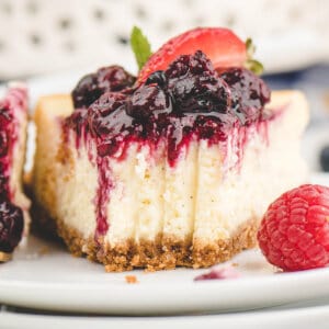 A slice of vanilla bean cheesecake topped with berry compote, a few bites missing