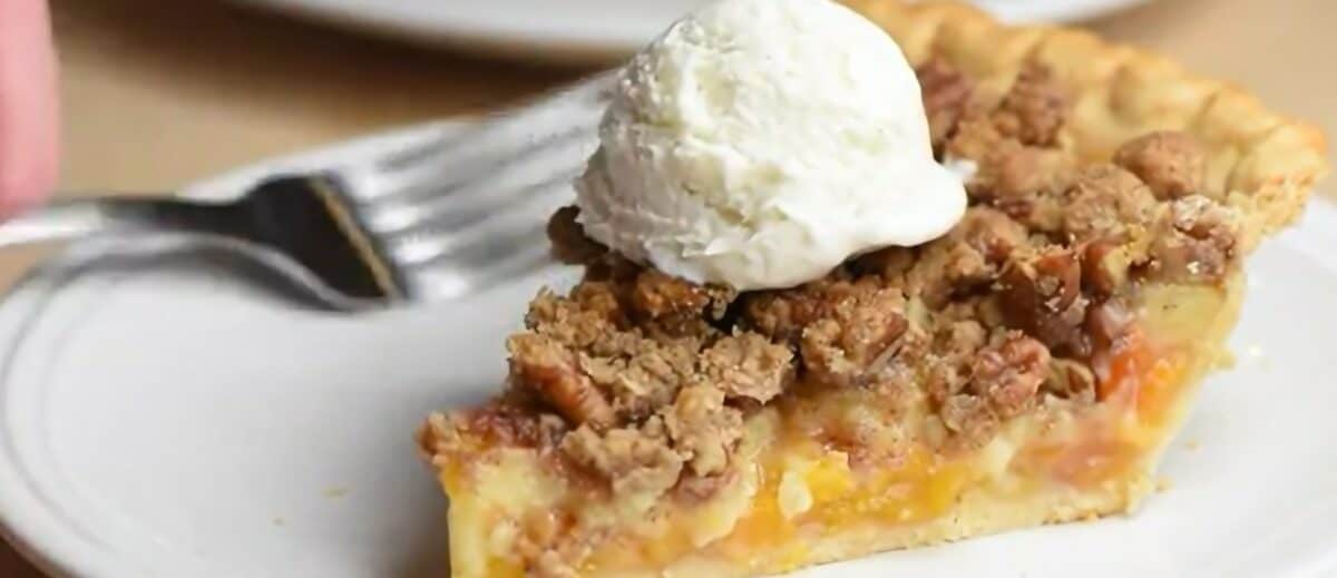 A slice of peach pie with a scoop of vanilla ice cream on top on a plate with a fork. 