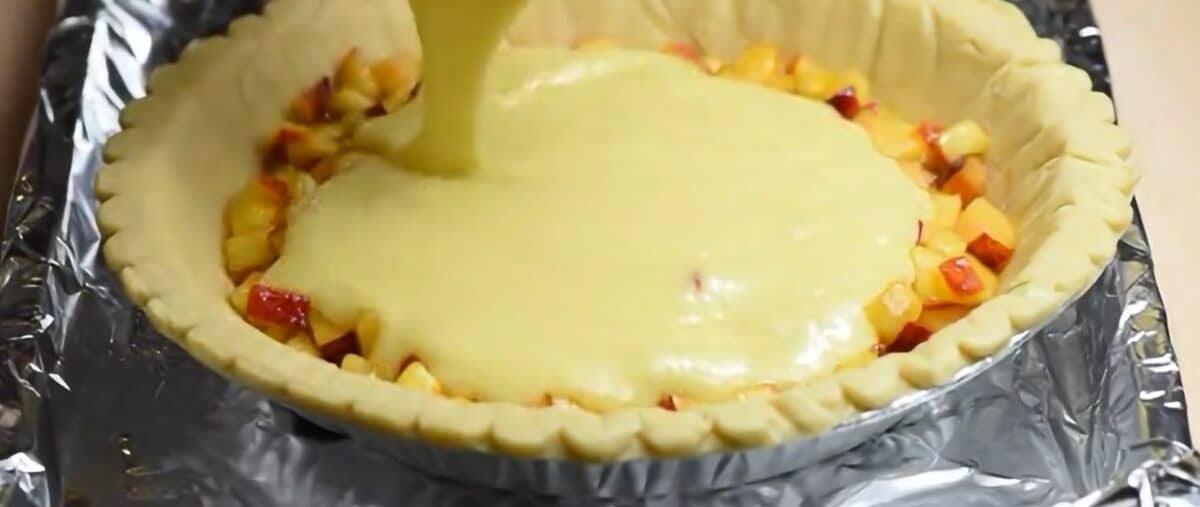 Pouring the custard over the peaches in the pie crust. 