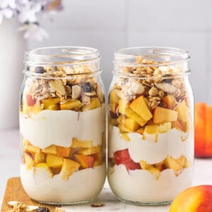 2 glass jars filled with layers of yogurt, peaches, and granola