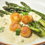 Angled view of a plate of scallops with pesto cream and asparagus