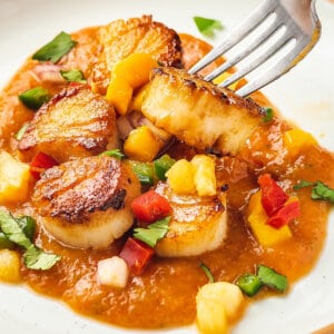 A fork stabbing a scallop in fruit sauce