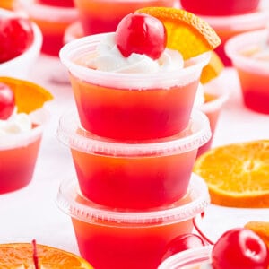 stack of 3 tequila sunrise jello shots garnished with whipped cream and a cherry