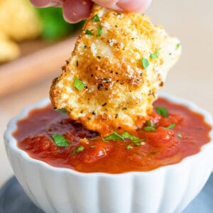 one toasted ravioli being dipped in marinara sauce