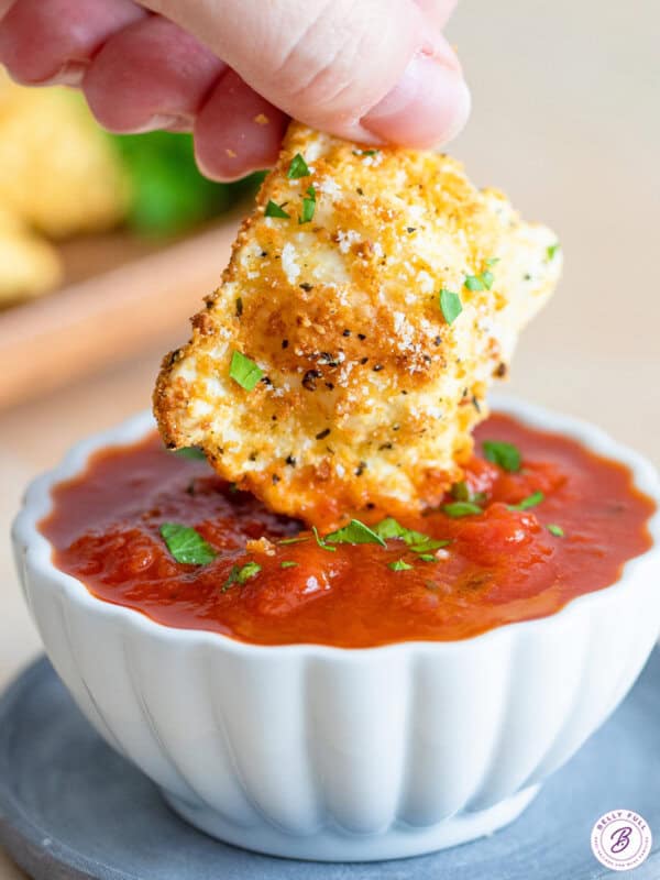 one toasted ravioli being dipped in marinara sauce