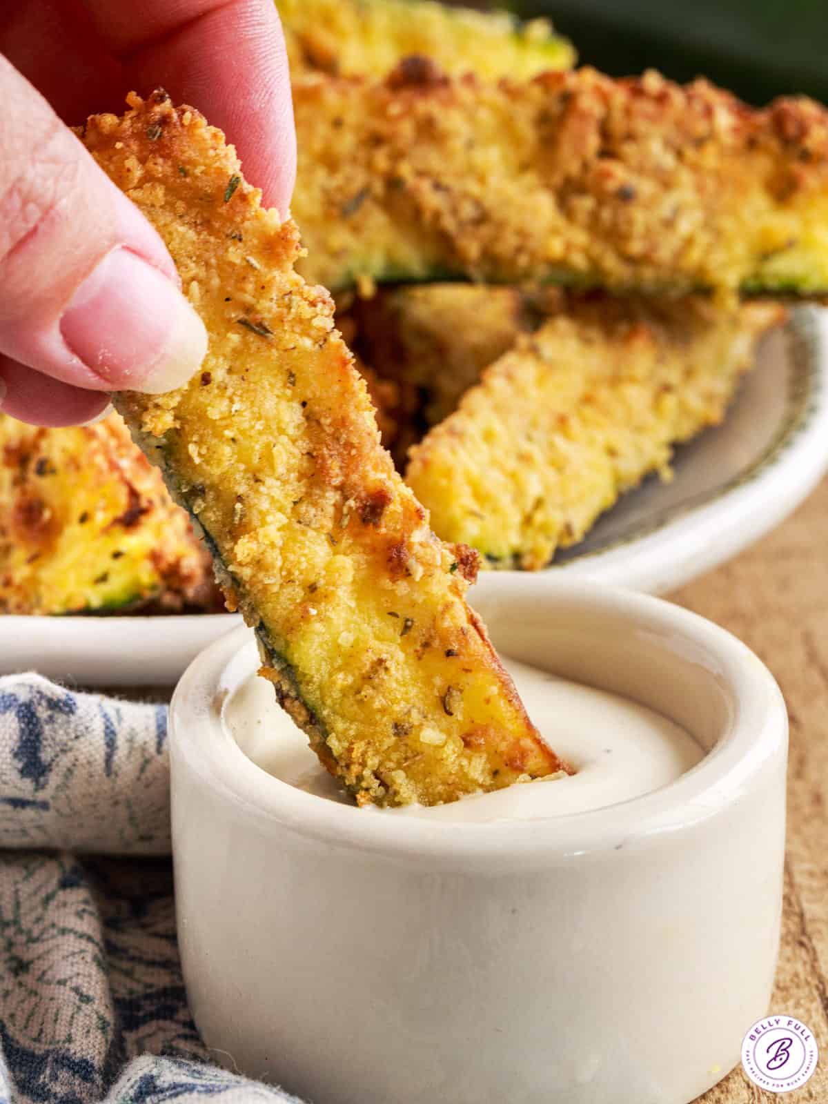 hand dipping breaded zucchini wedge in ranch dressing