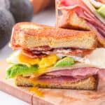 A ham and cheese sandwich with avocado, bacon, and egg on brioche bread