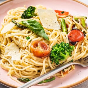 Angled view of a plate of pasta primavera with tomatoes, parmesan, and broccoli.