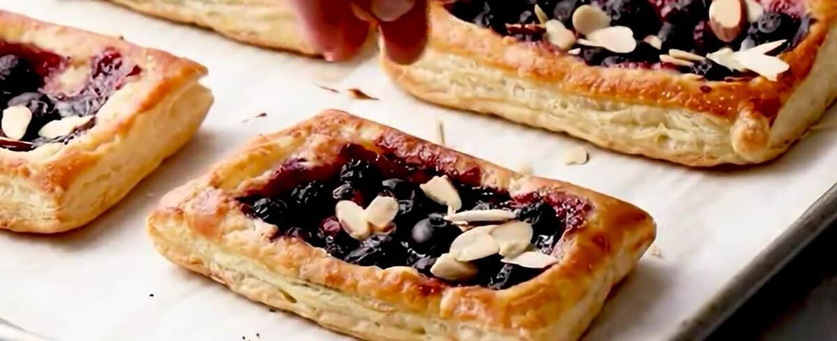Sprinkling almonds over the baked puff pastry tarts.