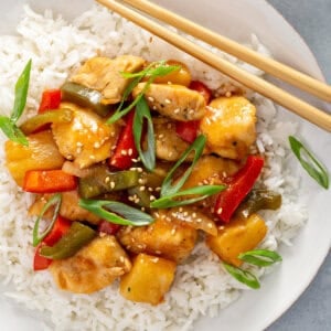 overhead sweet and sour chicken over rice on plate with chopsticks