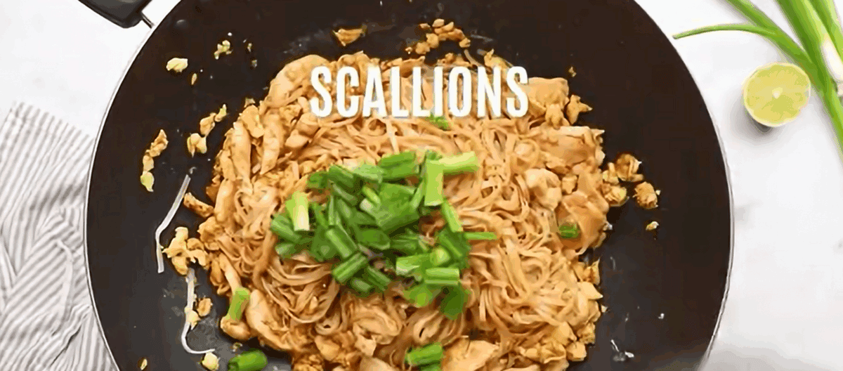 Adding scallions to the wok with the chicken, noodles, and eggs.