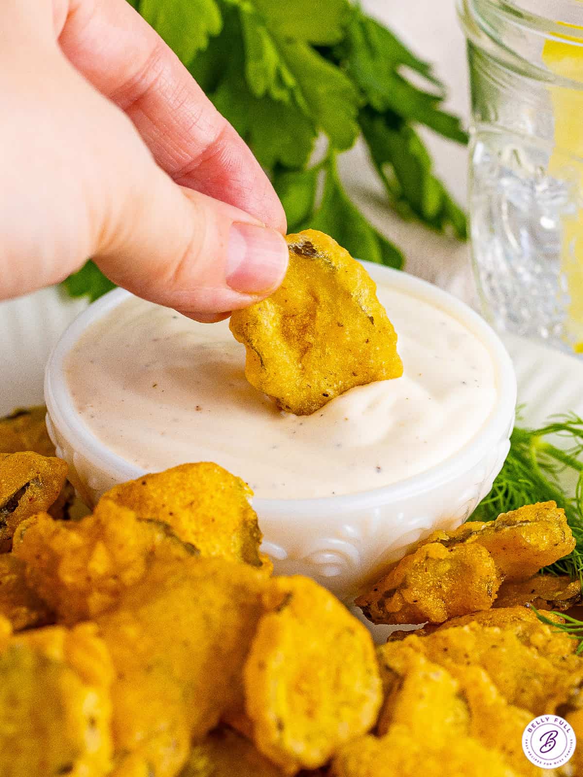 A hand dipping a fried pickle into ranch dressing