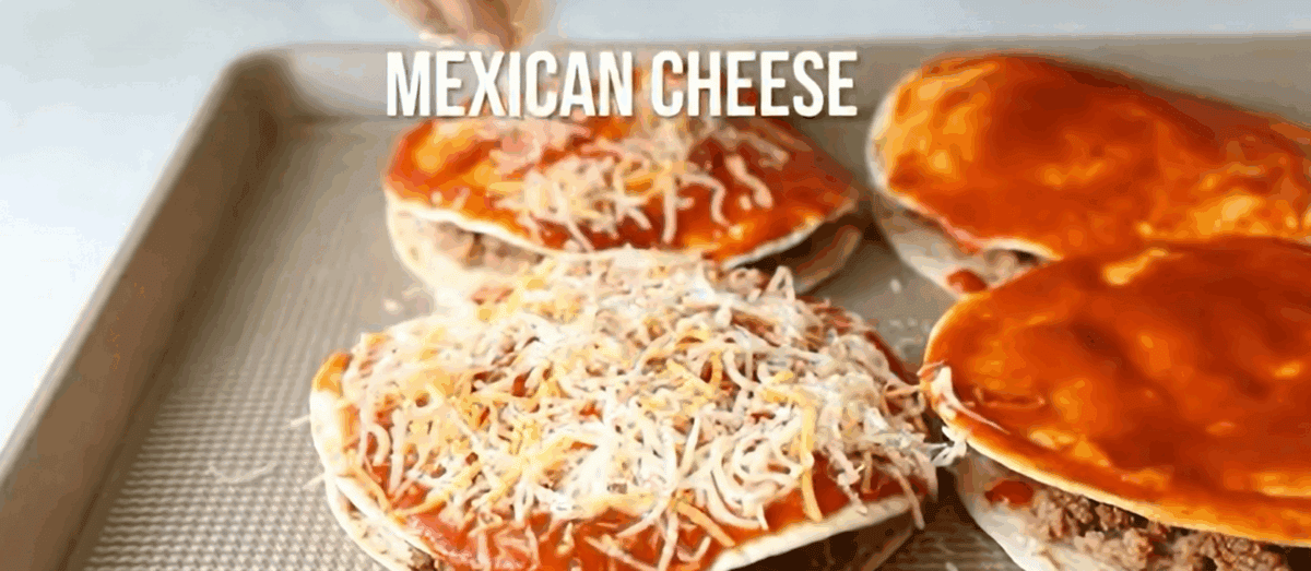 Tortillas stuffed with meat and beans being topped with sauce and cheese.