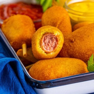 Mini corn dogs in a serving try, one with a bite missing