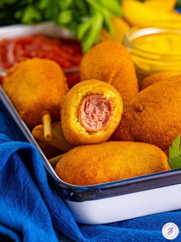 Mini corn dogs in a serving try, one with a bite missing