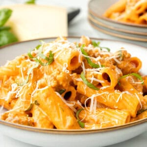 creamy sausage pasta on plate with parmesan and basil