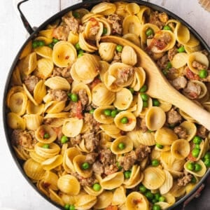 overhead sausage and pea pasta in skillet with serving spoon