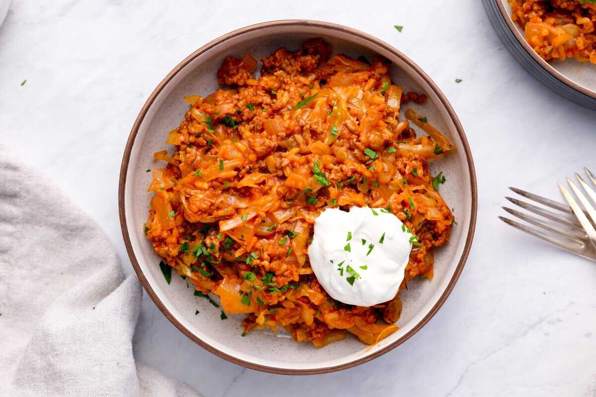 A bowl of unstuffed cabbage rolls with a dollop of sour cream.