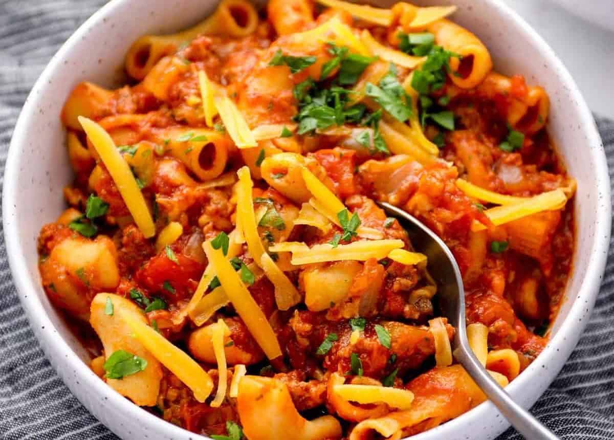 American goulash in a bowl with cheese, parsley, and a spoon.