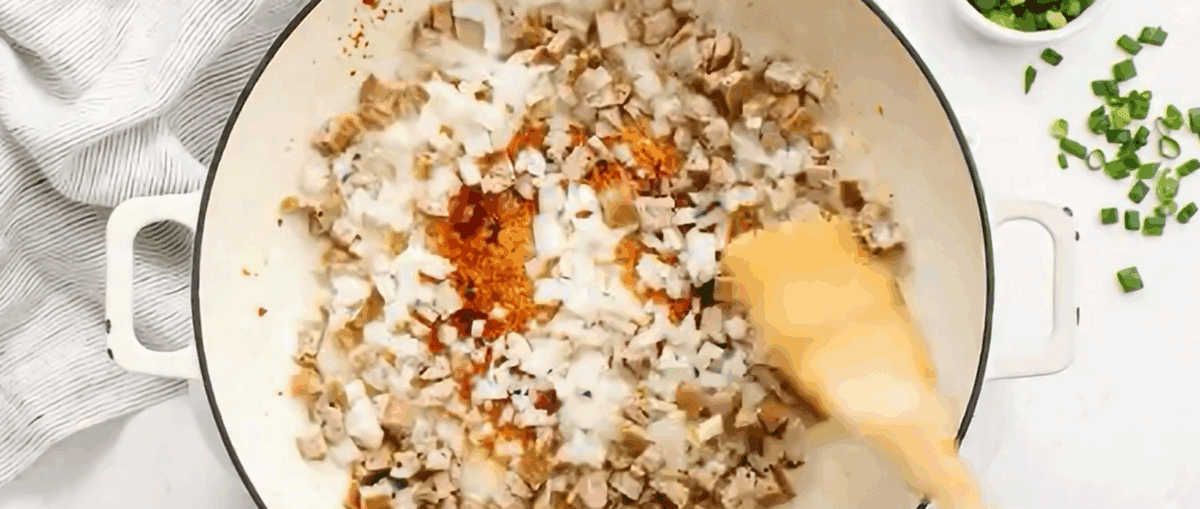 Cooking onion and chicken sausage in a white skillet.