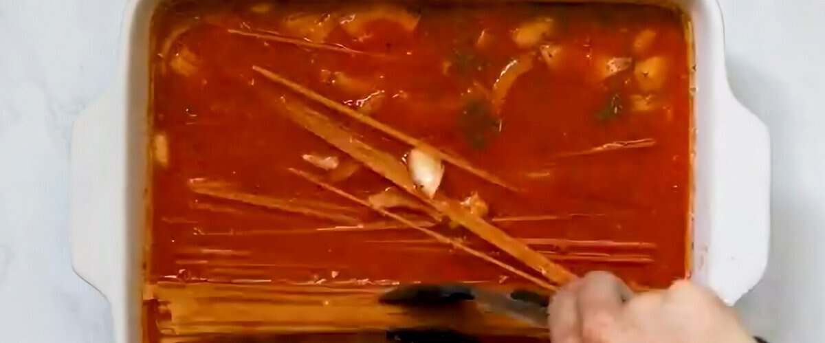 Ingredients to make baked spaghetti in the baking pan being stirred.