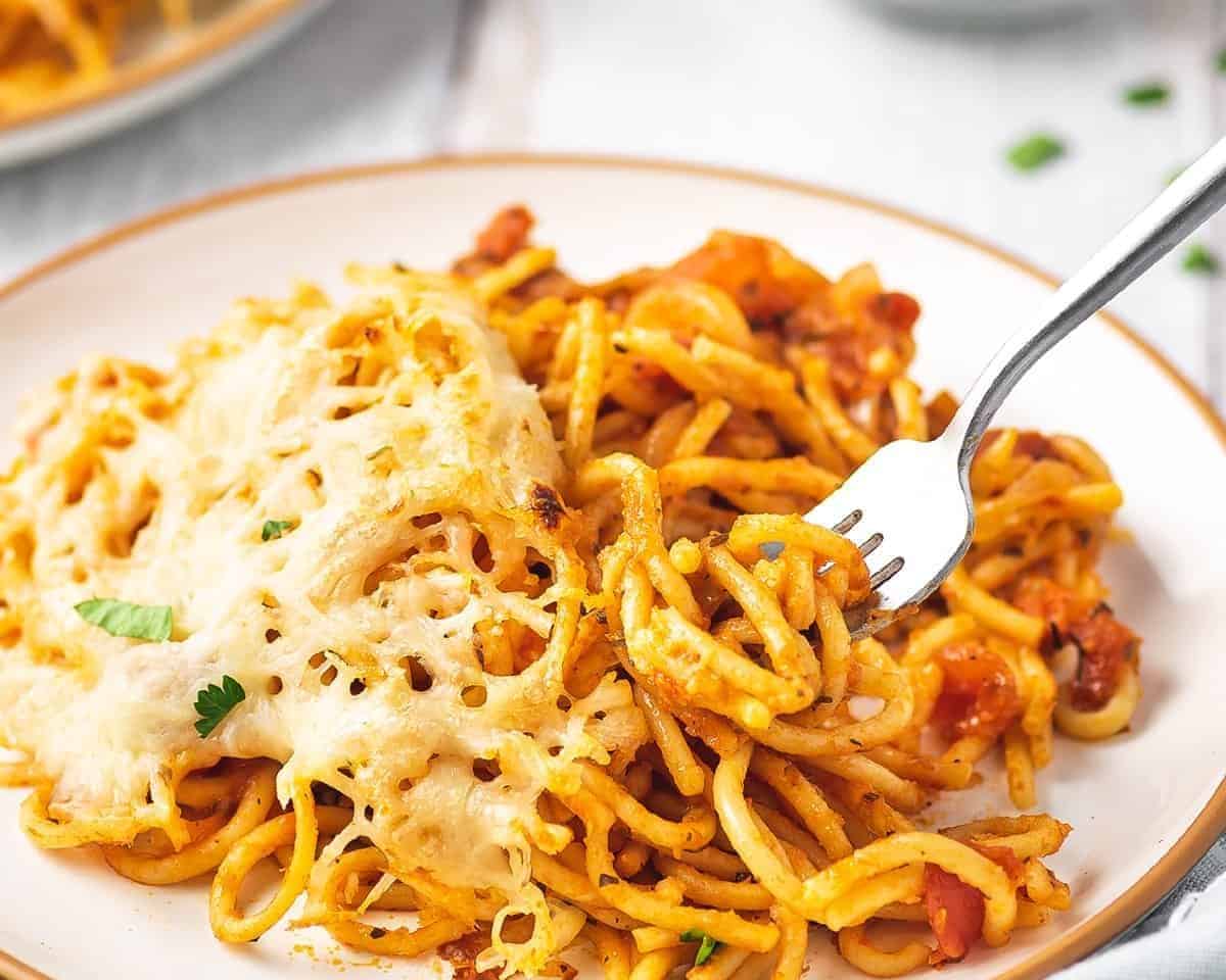 There's no need to pre-cook the pasta in this Easy Baked Spaghetti Recipe. Just toss it with the sauce, add broth, & bake! Baked spaghetti on a plate with a fork.