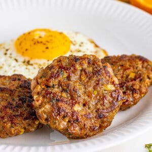 Three breakfast sausage patties on a white plate with a fried egg